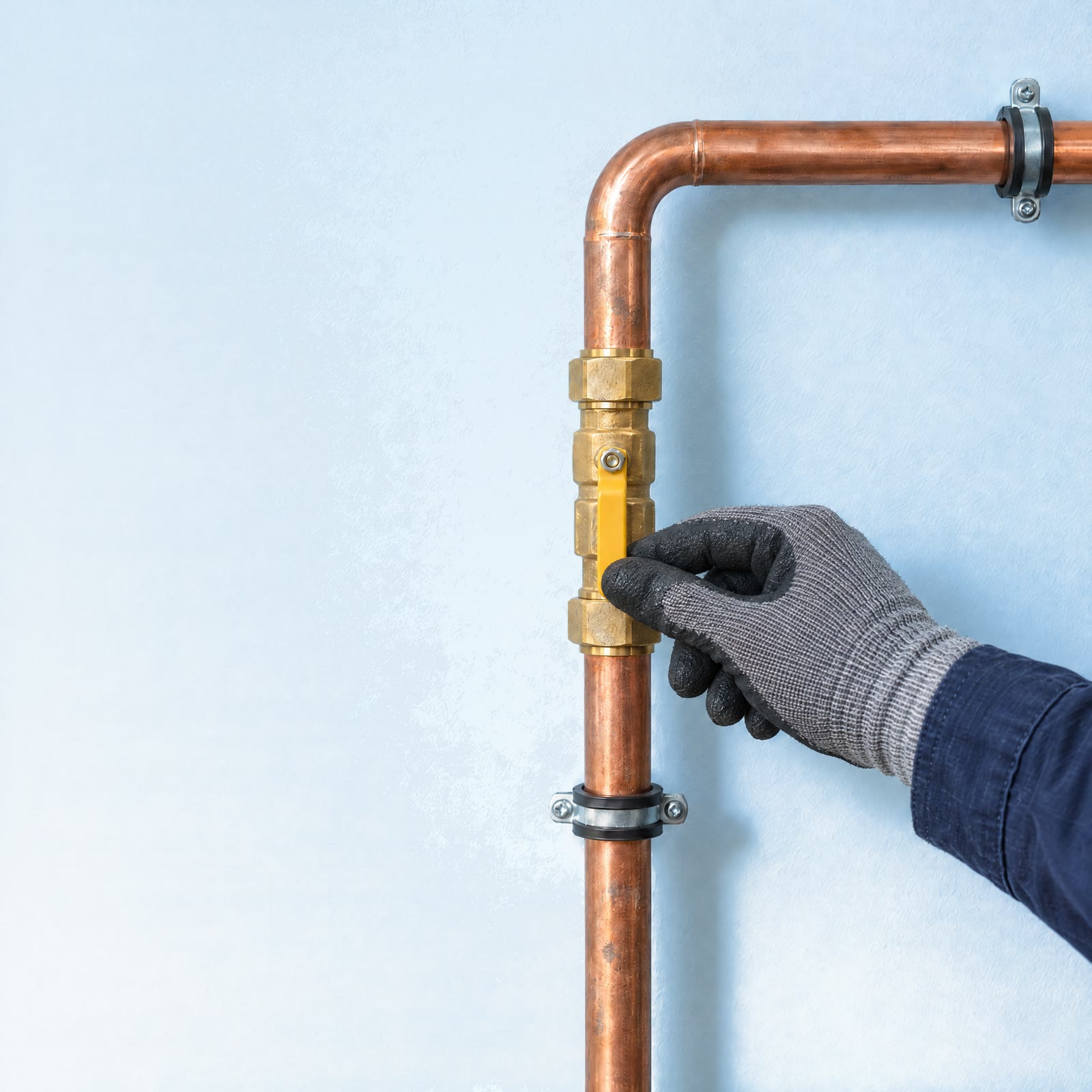 Hand im Arbeitshandschuh am gelben Hebel des Gashahns einer neuen Gasleitung aus Kupfer
