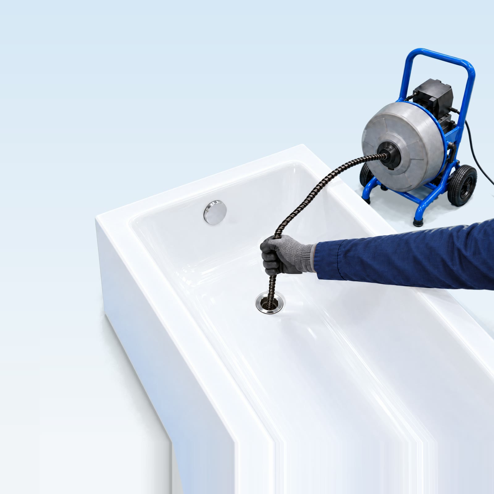 Installateur führt die Spirale einer Rohrreinigungsmaschine in den Abfluss einer Badewanne